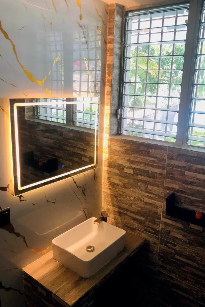 Lavabo blanco sobre encimera de madera maciza, con espejo retroiluminado y celosía de ventana al fondo