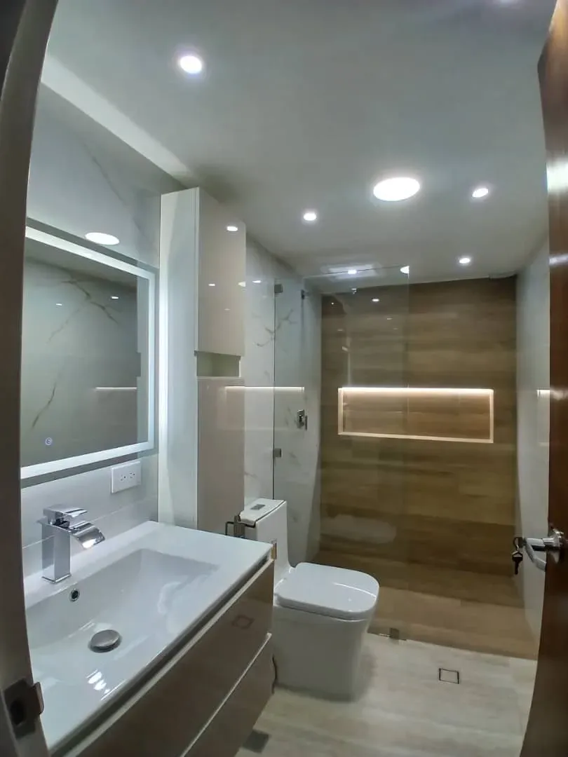 Baño principal con espejo retroiluminado, lavamanos de superficie continua y ducha con revestimiento de madera