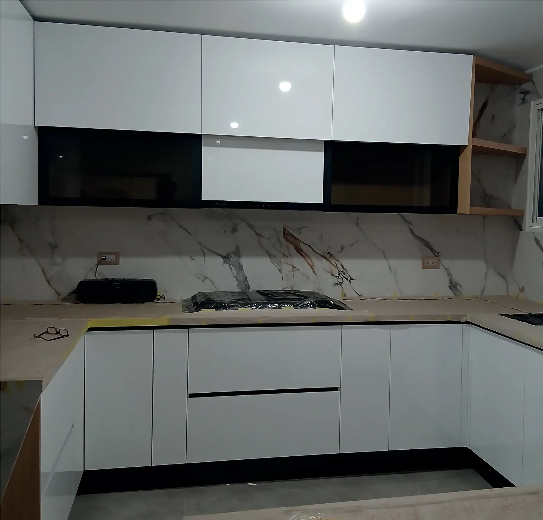 Cocina en obra con muebles blancos sin tiradores y salpicadero de porcelanato veteado tipo mármol
