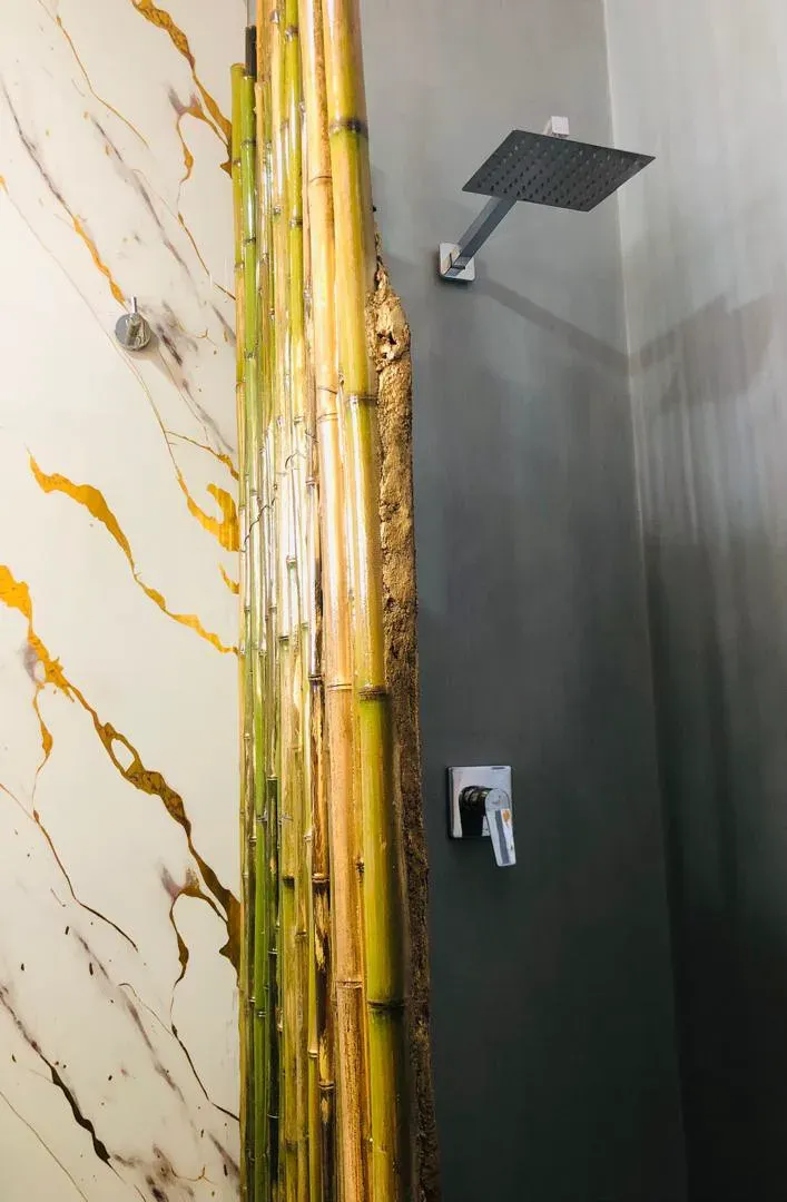 Ducha empotrada con grifería y rociador en acabado negro mate sobre revestimiento gris, junto a panel de bambú
