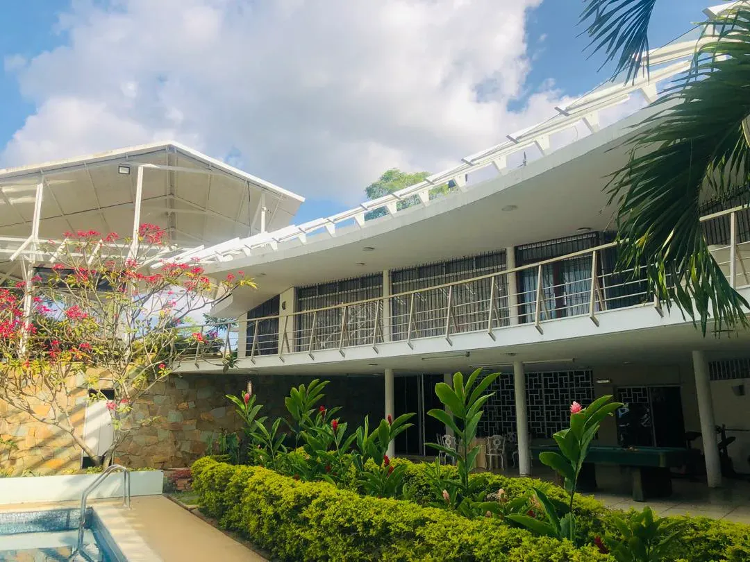Exterior de la residencia diplomática: fachada blanca de dos niveles con jardín tropical y buganvilla en flor