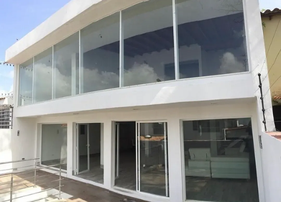 Fachada posterior de la Quinta Mangore con muro cortina de vidrio en la planta alta y ventanales corredizos abajo