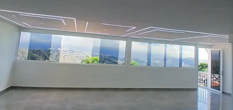 Salón principal con ventanal corrido de piso a techo e iluminación lineal empotrada en el cielo raso